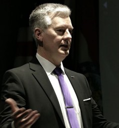 Dr. Jim Burkee in suit and tie, speaking with hand gestures.