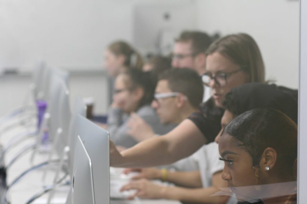 A diverse group of men and women students at computers in a classroom.