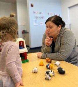 A staff member uses her hands to interact with a toddler as they play with farm animal toys together.